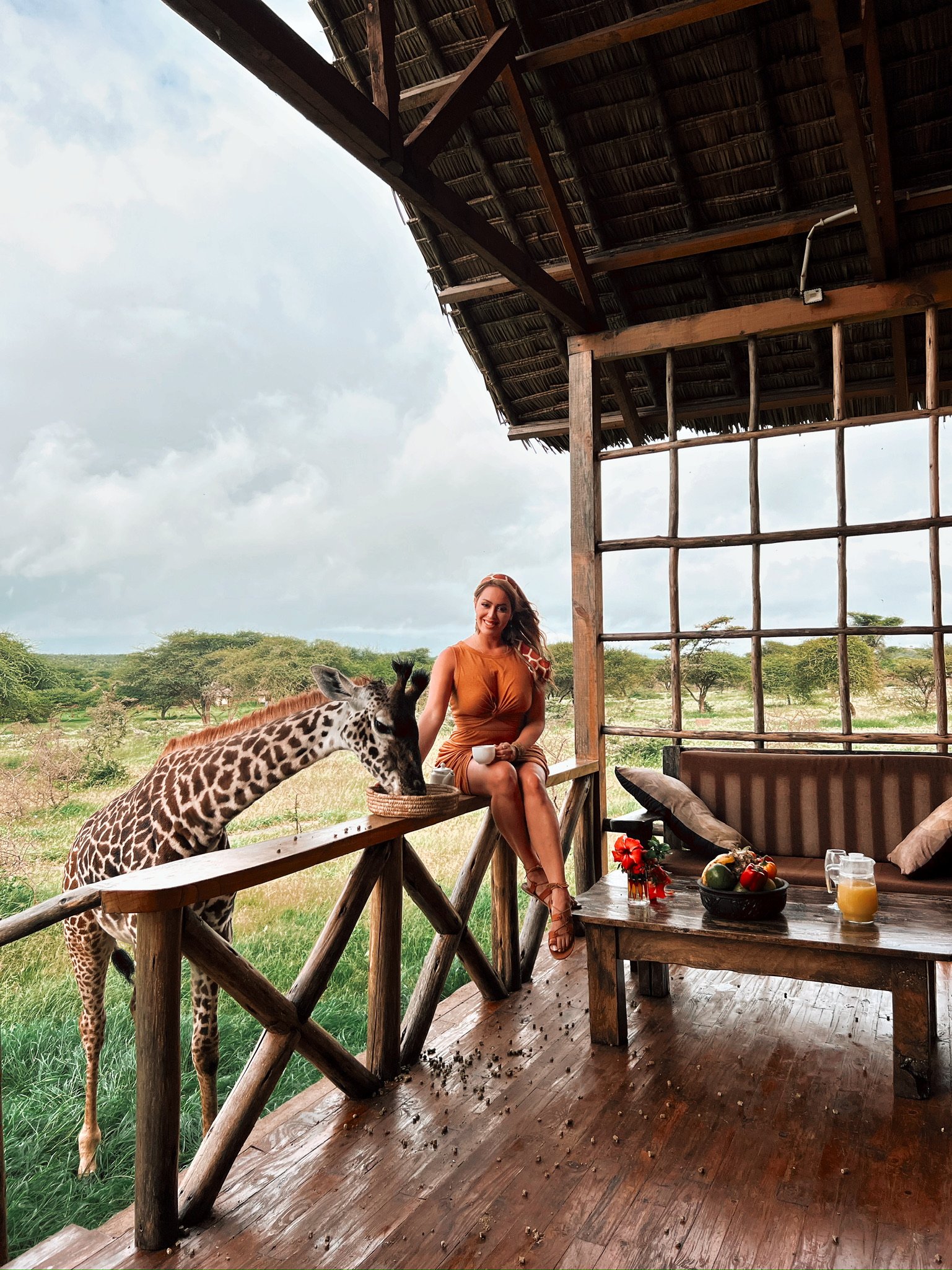 Guest on a thatched villa veranda beside a giraffe at Serval Wildlife