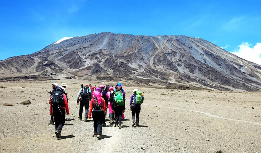 Trekkers approaching Kilimanjaro across rocky alpine terrain
