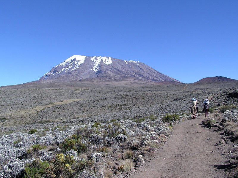 Pico Kibo acima de um trilho rochoso com caminhantes ao longe