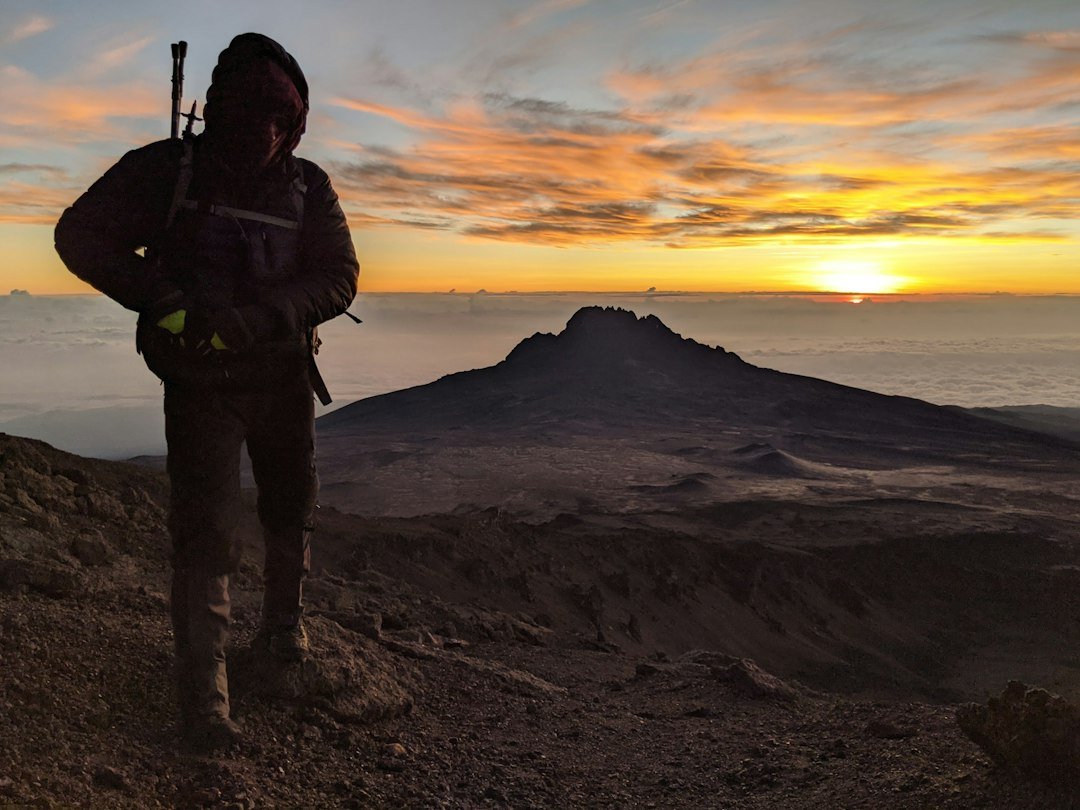 Randonneur sur le Kilimandjaro devant un ciel orangé au coucher du soleil